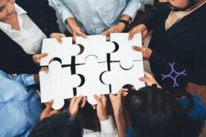 Diverse corporate officer workers collaborate in office, connecting puzzle pieces to represent partnership and teamwork. Unity and synergy in business concept by merging jigsaw puzzle. Concord